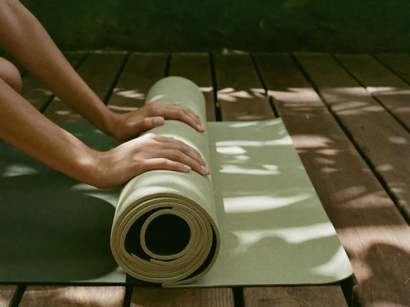 AI-generated close-up of hands resting on a rolled linen mat on teak boards in dappled shade