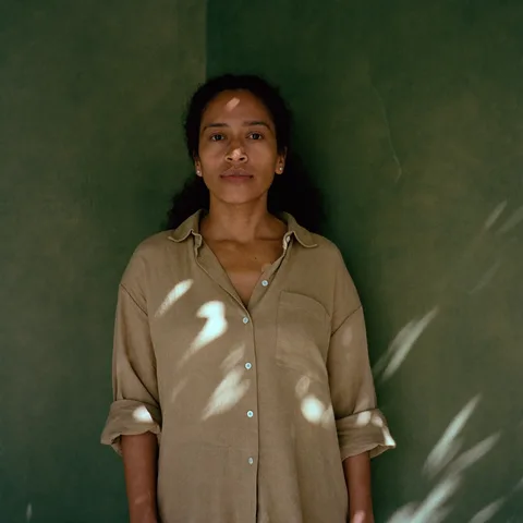 AI-generated portrait of Marisol, a fictional teacher, in a sand linen shirt against a green plaster wall